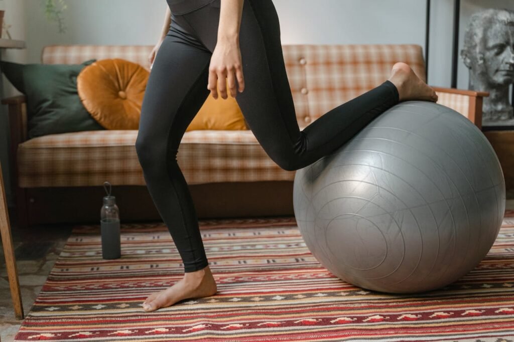 Woman performing home exercise routine using an exercise ball, wearing black leggings.